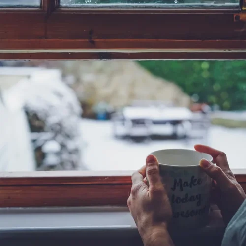 A person holding a warm mug by a window, illustrating comforting gifts for a grieving friend