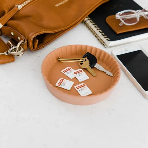 Leather valet tray holding keys with AirTag, wallet, and phone on wooden surface
