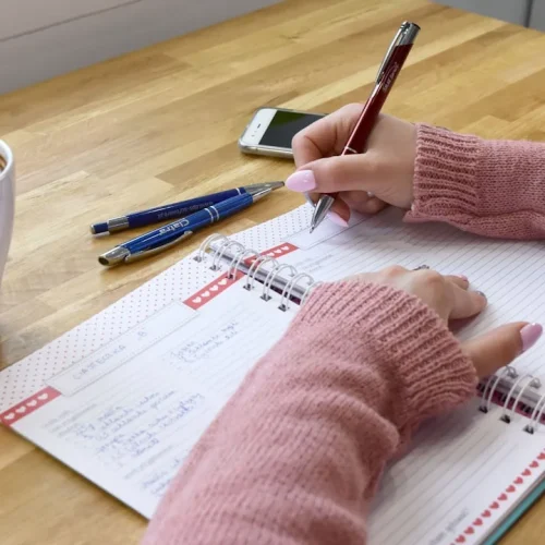 Journaling supplies including an open notebook, fountain pen, ink, and washi tape arranged on a wooden desk