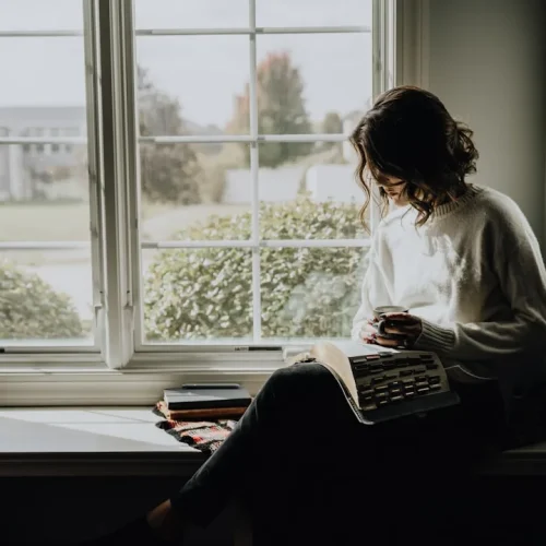 Quiet person enjoying a book by a sunlit window in a calm, comfortable home setting