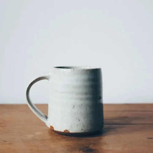 Hand-thrown ceramic mug beside folded linen handkerchief and leather journal on wooden surface